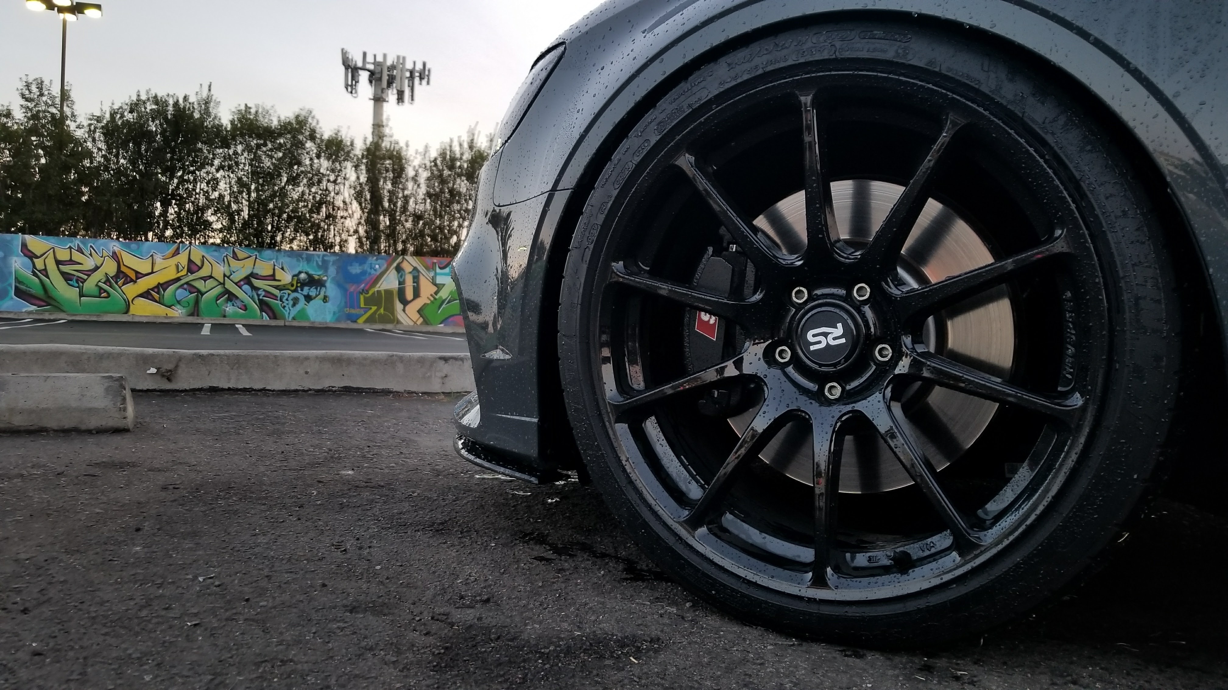 Black RS wheel on wet asphalt, graffiti wall in the background