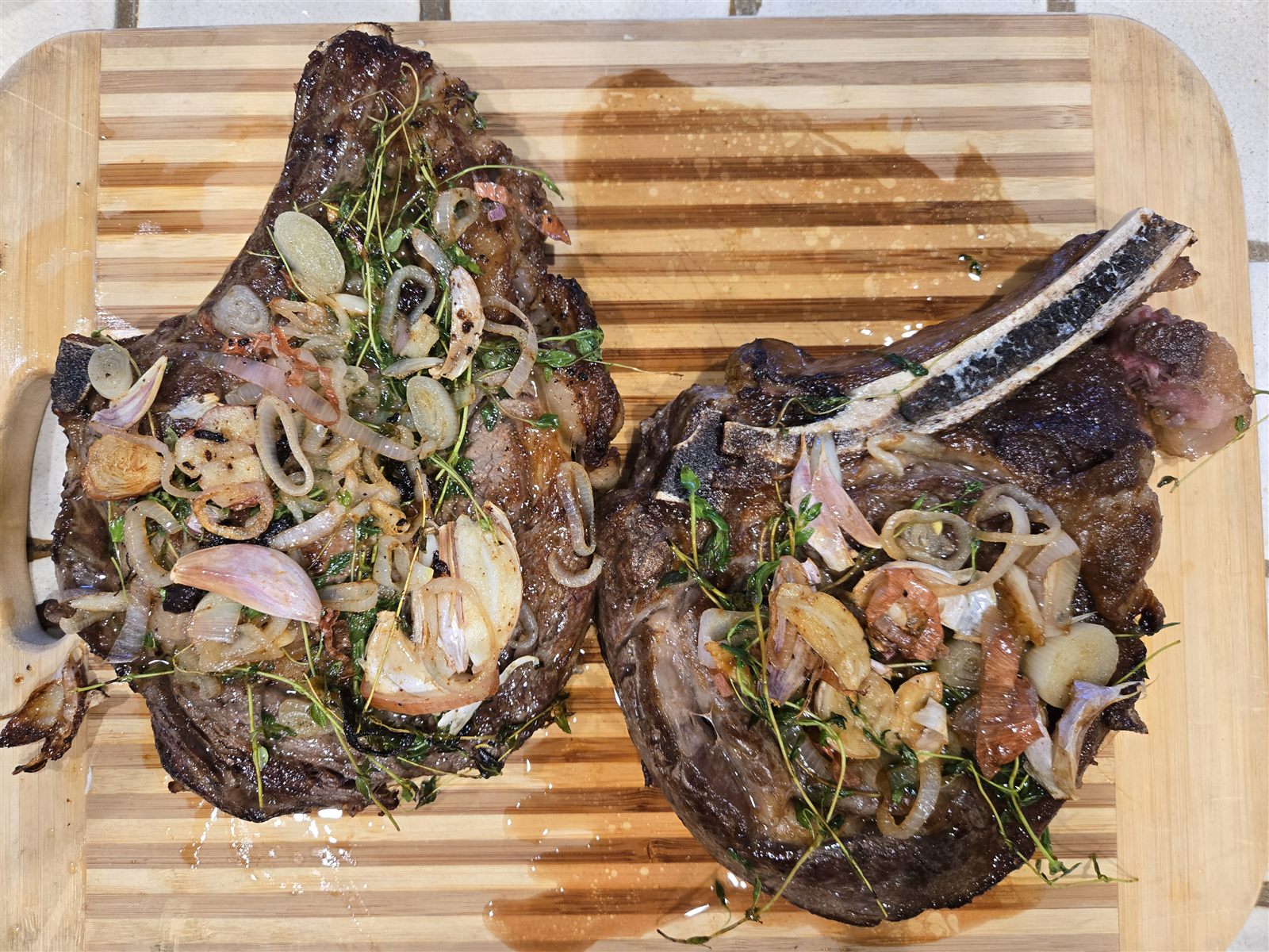 Cooked bone-in ribeyes resting with shallots and herbs